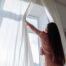 A woman opening the curtains to let natural light into the room.