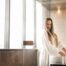 A woman standing near the tinted bathroom window, washing her hands at the sink.
