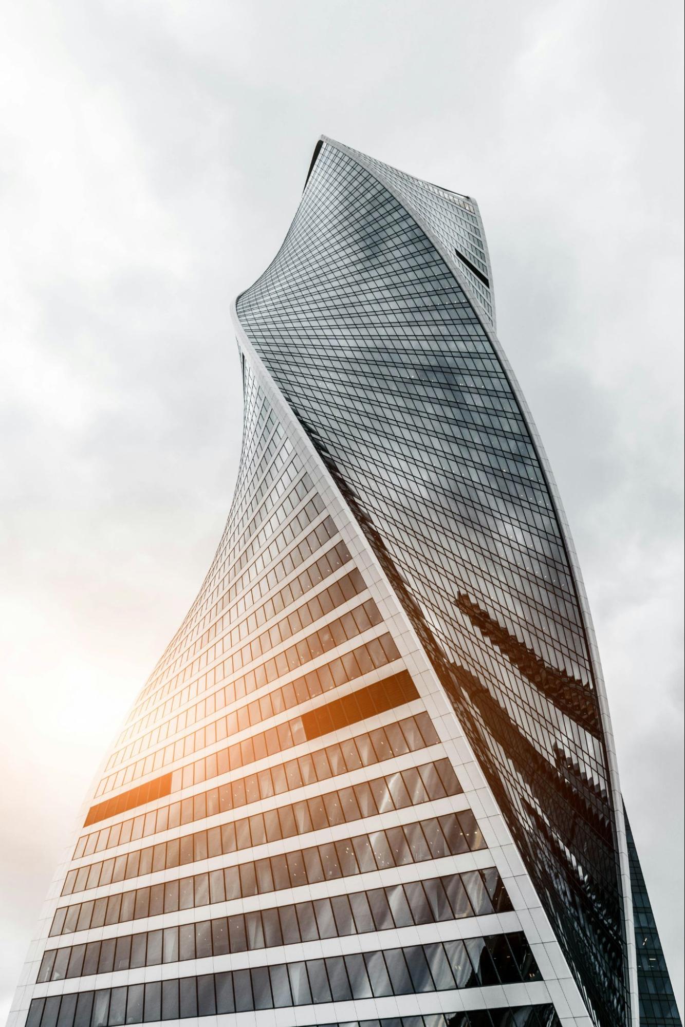 Sunlight reflects off the glass of a beautiful high rise featuring a curved construction.