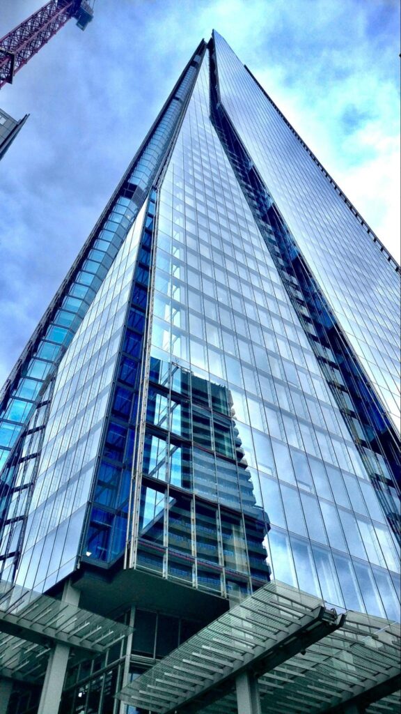 A high rise reflects the nearby buildings and the surrounding blue skies from extensive windows in the facade.