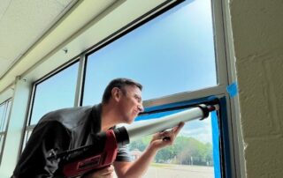 One of the members of the AP Corp team working on a security window film installation in a school.