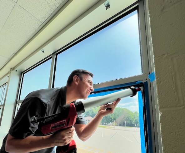 One of the members of the AP Corp team working on a security window film installation in a school.