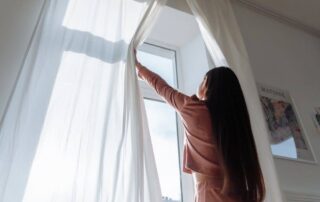 A woman opening the curtains to let natural light into the room.