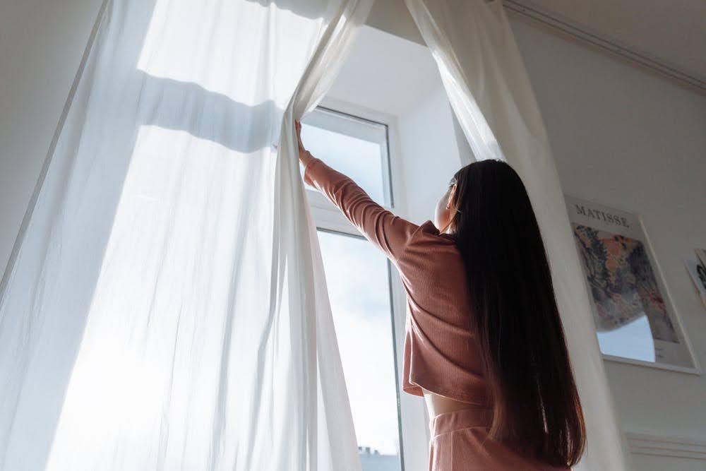 A woman opening the curtains to let natural light into the room.