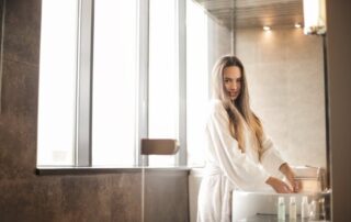 A woman standing near the tinted bathroom window, washing her hands at the sink.