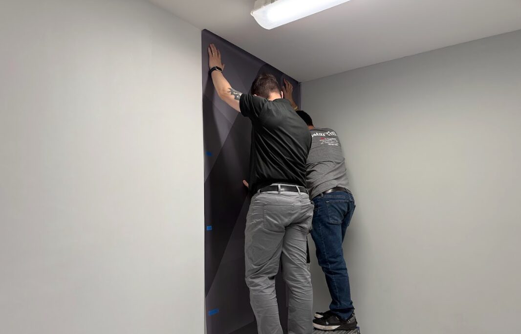 Solar Tint team installing custom wayfinding wall graphics in a hall.